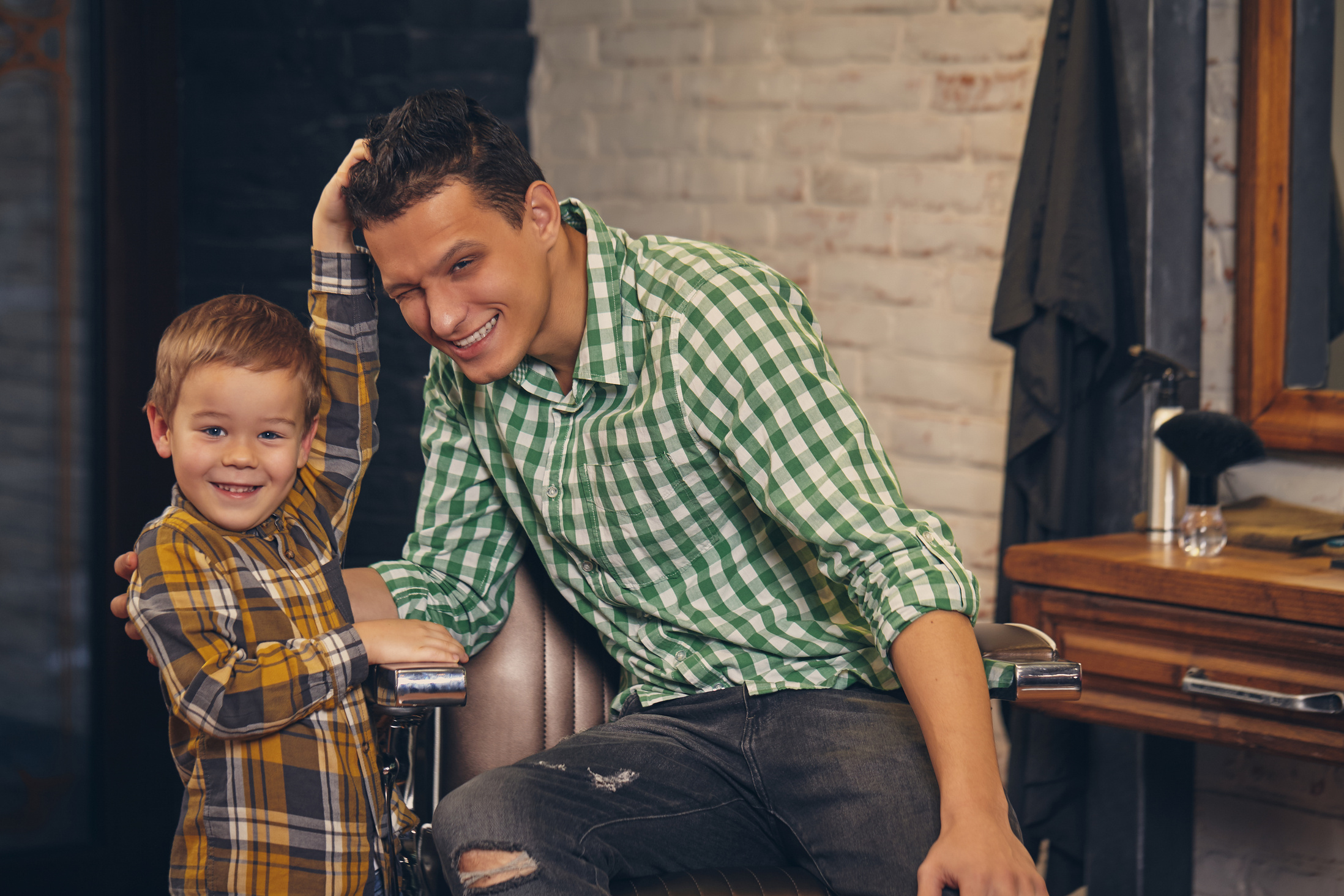 Young Handsome Father and His Little Stylish Son at Barbershop Waiting for Barber